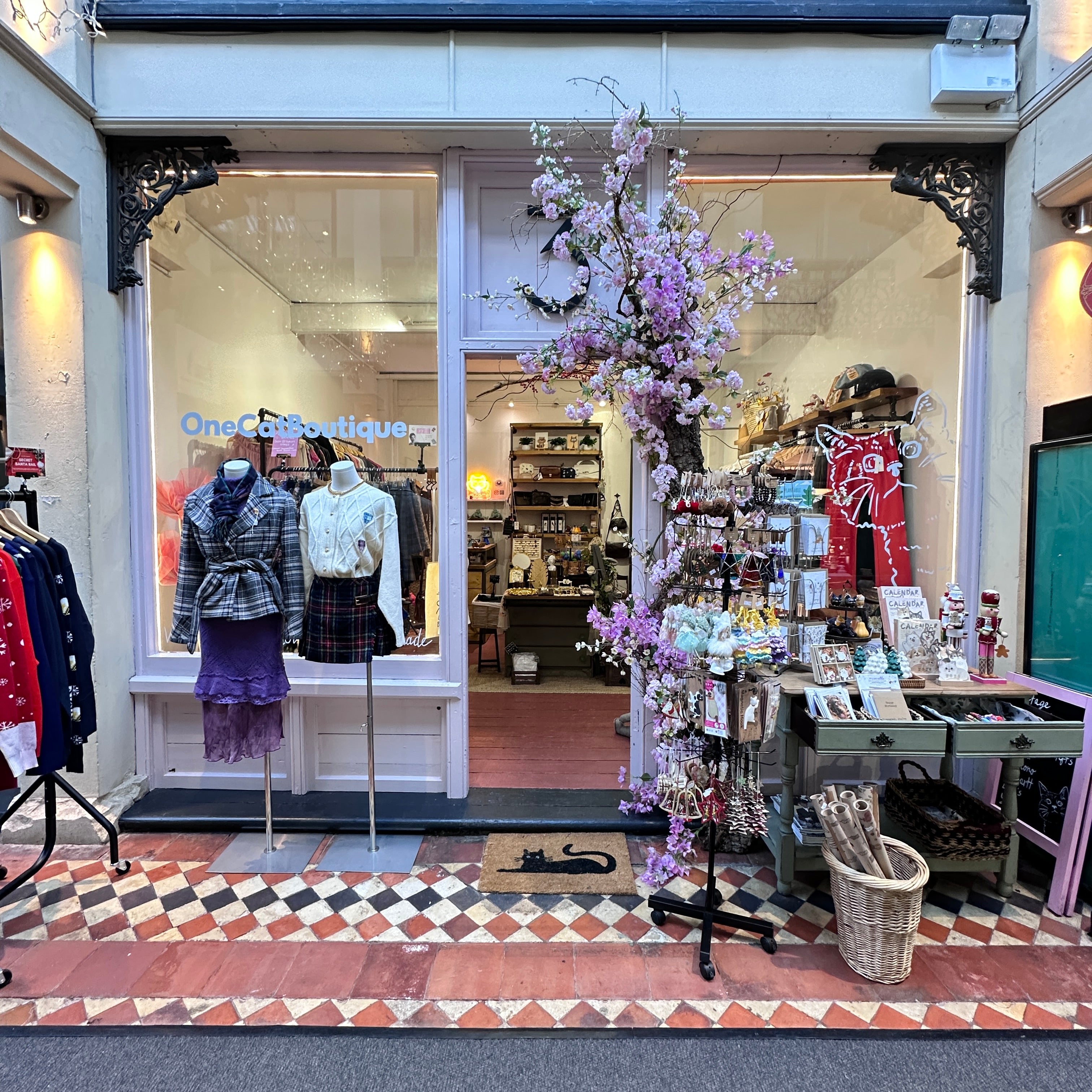 Storefront with floral display and mannequins inside, on a street with decorative tiles.
